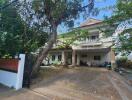 Large two-story house with drive under a tree