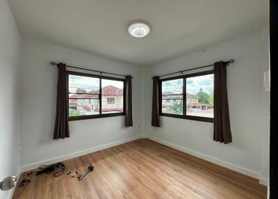 A bright and empty bedroom with two large windows and wooden flooring