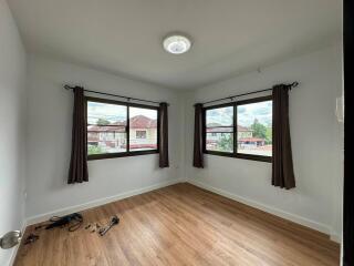 A bright and empty bedroom with two large windows and wooden flooring