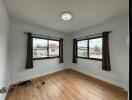 A bright and empty bedroom with two large windows and wooden flooring