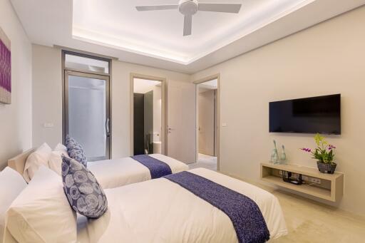 Modern bedroom with two single beds, ceiling fan, and a wall-mounted TV