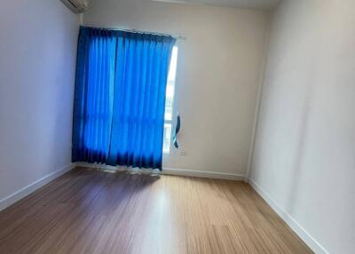 Empty bedroom with wooden flooring, blue curtains, and a ceiling light