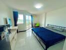 Bright bedroom with a double bed, a TV, a desk with a green chair, and a large window leading to a balcony