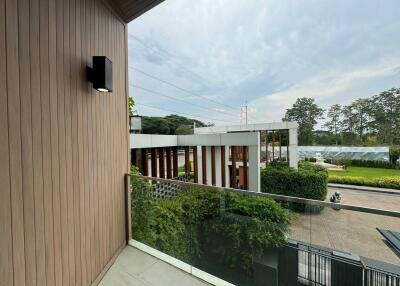 Modern balcony with a wooden wall, glass railing, and views of greenery and buildings