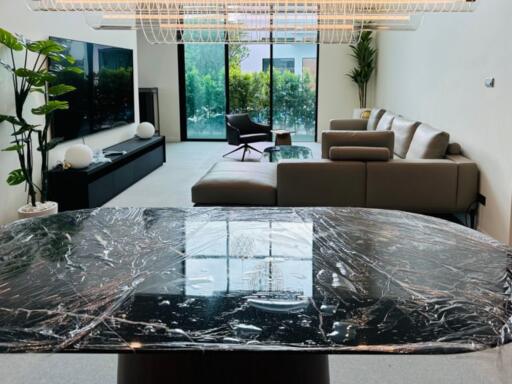 Modern living room with a marble coffee table, large sofa, flat screen TV, and large windows.