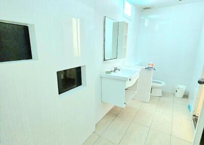 Modern bathroom with white tiles, sink, toilet, and storage shelves