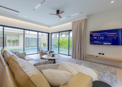 Modern living room with large windows, beige sofa, wall-mounted TV, and pool view