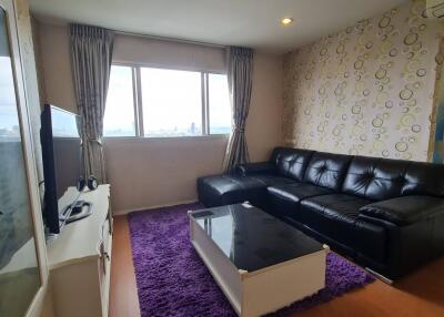 Living room with black leather sofa, coffee table, purple rug, TV, and city view