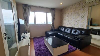 Living room with black leather sofa, coffee table, purple rug, TV, and city view