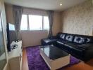 Living room with black leather sofa, coffee table, purple rug, TV, and city view