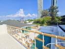 A spacious balcony with a wide view of the city including high-rise buildings, greenery, and a swimming pool below