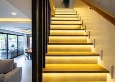 Modern interior stairway with illuminated steps leading to upper floor, view of living room and dining area