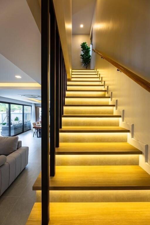 Modern interior stairway with illuminated steps leading to upper floor, view of living room and dining area