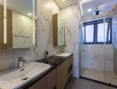 Modern bathroom with double sinks, shower, and large windows