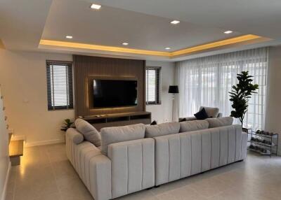 Modern living room with large sofa, flat-screen TV, and ample lighting