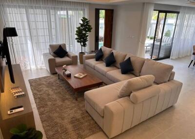 Modern living room with large sofa, coffee table, plants, and large windows