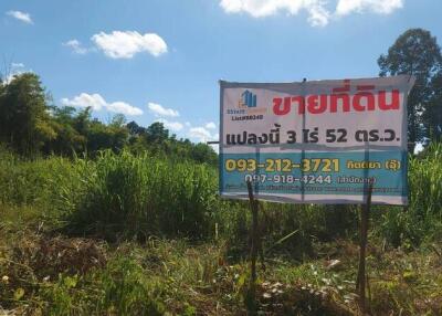 Land for sale with contact information in front of greenery and trees