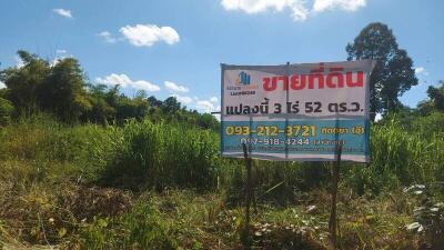 Land for sale with contact information in front of greenery and trees