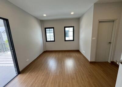 Empty bedroom with wooden flooring, two windows, and a balcony door.