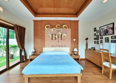 Spacious and well-lit bedroom with wooden flooring and ceiling finish, featuring a large bed and sliding glass doors leading to a garden.