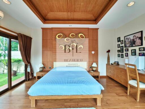 Spacious and well-lit bedroom with wooden flooring and ceiling finish, featuring a large bed and sliding glass doors leading to a garden.