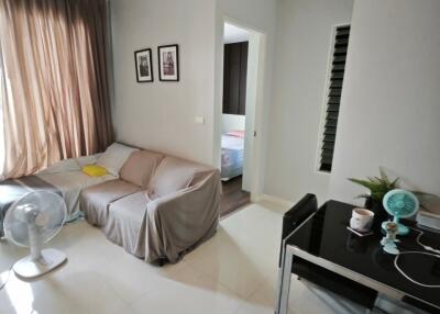 Modern living room with a sofa, fan, desk, and view into a bedroom