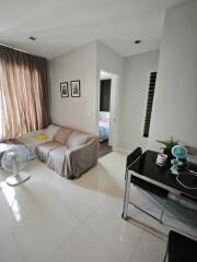 Modern living room with a sofa, fan, desk, and view into a bedroom