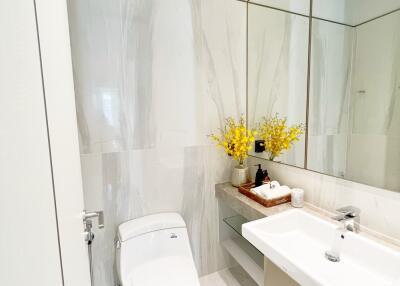 Modern bathroom with toilet and sink, large mirror, and decorative yellow flowers.