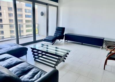 Modern living room with glass coffee table, black leather furniture, and large windows