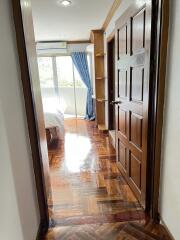 Bedroom with wooden flooring and door, blue curtains, and a window view