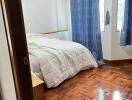 Cozy bedroom with wooden floors, white walls, and blue curtains