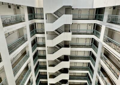 Photo of a multi-story building with a central staircase and parked cars at the ground floor.