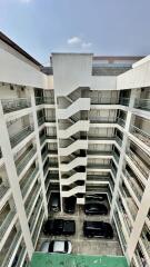 Photo of a multi-story building with a central staircase and parked cars at the ground floor.