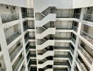 Photo of a multi-story building with a central staircase and parked cars at the ground floor.