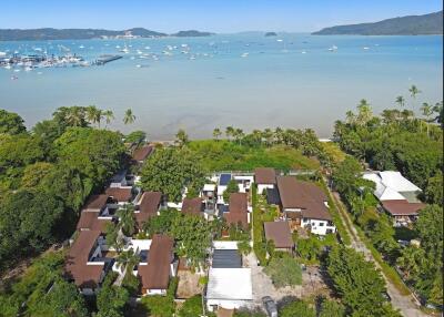 Aerial view of beachfront property with multiple buildings, lush greenery, and a bay with anchored boats