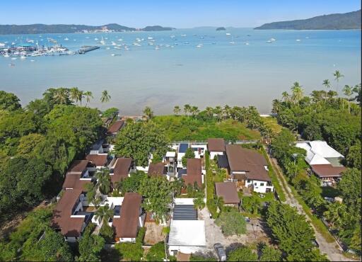 Aerial view of beachfront property with multiple buildings, lush greenery, and a bay with anchored boats