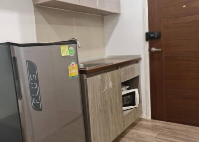 Compact kitchen area with wood cabinets, mini fridge, microwave, and wooden flooring