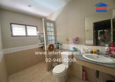 Bathroom with tiled walls, a toilet, a sink with a countertop, a mirror, and shelves with toiletries.