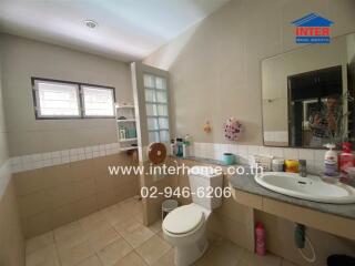 Bathroom with tiled walls, a toilet, a sink with a countertop, a mirror, and shelves with toiletries.