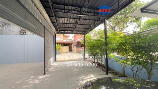 Covered parking area with view of garage door, greenery, and neighboring houses