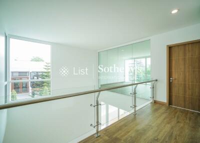 Modern hallway with wooden flooring, glass railing, and a wooden door