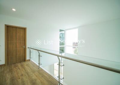 Bright upper hallway with wooden floor, glass railing, and a wooden door