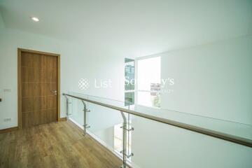 Bright upper hallway with wooden floor, glass railing, and a wooden door