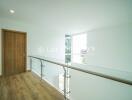 Bright upper hallway with wooden floor, glass railing, and a wooden door