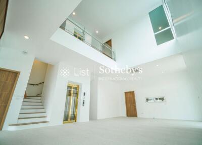 Spacious and modern living area with high ceiling and a mezzanine, featuring large windows, a staircase, and a wooden door.