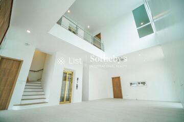 Spacious and modern living area with high ceiling and a mezzanine, featuring large windows, a staircase, and a wooden door.