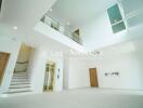 Spacious and modern living area with high ceiling and a mezzanine, featuring large windows, a staircase, and a wooden door.