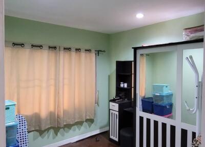 A well-lit bedroom with green walls, a window with beige curtains, and storage furniture