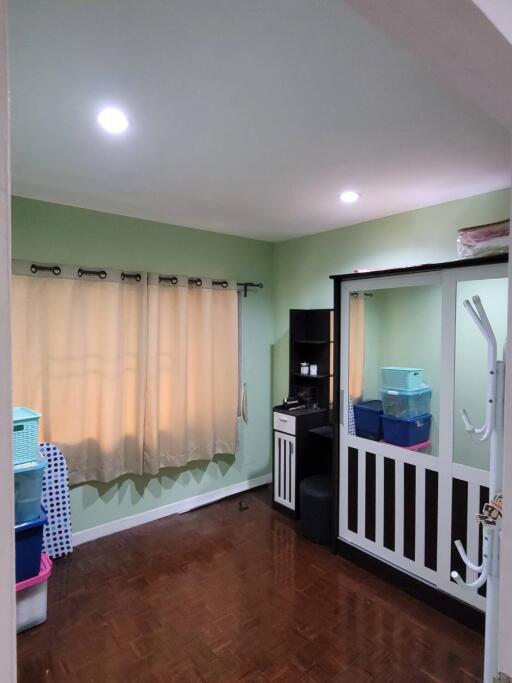 A well-lit bedroom with green walls, a window with beige curtains, and storage furniture