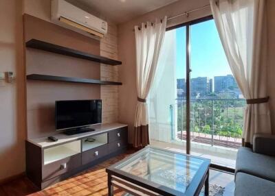 Modern living room with glass coffee table, wall-mounted TV, and a large sliding door opening to a balcony.